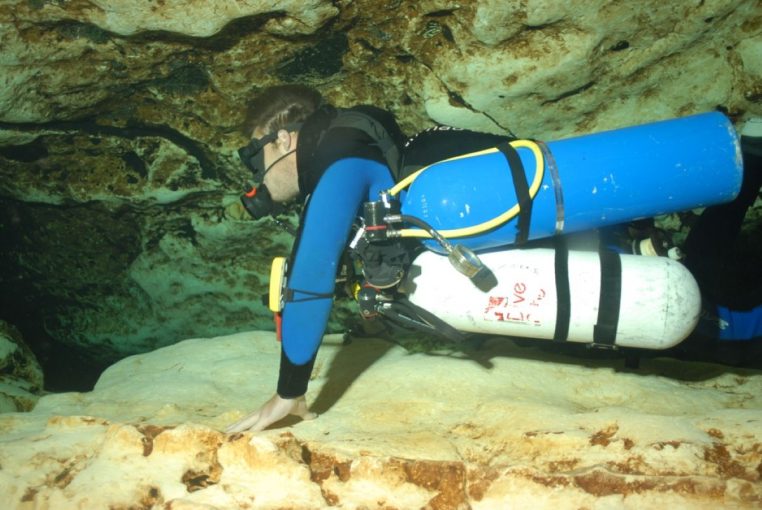 Plongeur en configuration sidemount dans une grotte, progression lente au plafond bas.