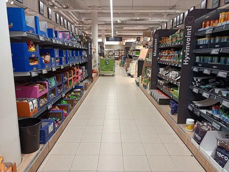 Allée de supermarché avec rayons remplis et perspective centrale, éclairage au plafond, ambiance de courses.