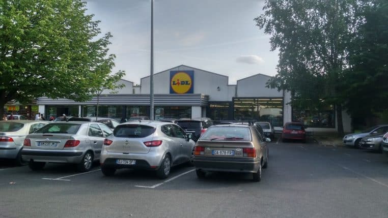 Entrée d’un supermarché Lidl à Paris avec voitures garées, logo au centre et façade vitrée en plan large.