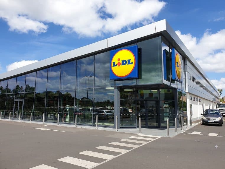 Magasin Lidl moderne avec grande façade vitrée, logo en angle, passage piéton au premier plan, ciel bleu.