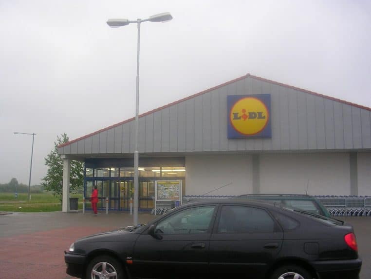 Façade d’un supermarché Lidl avec logo visible, entrée vitrée et parking au premier plan, vue de face.