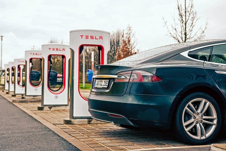 Tesla branchée à une borne Supercharger, connecteur visible et câble tendu, scène de recharge en extérieur.