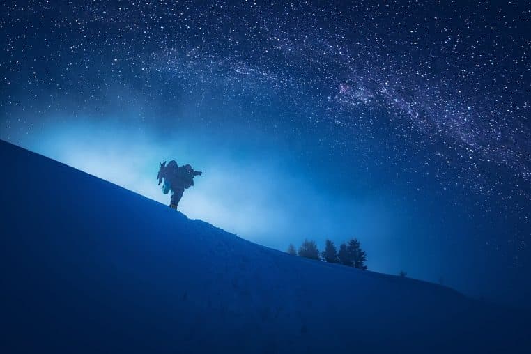 Silhouette d’un photographe sur une pente enneigée sous un ciel étoilé, voie lactée visible, nuit d’hiver.