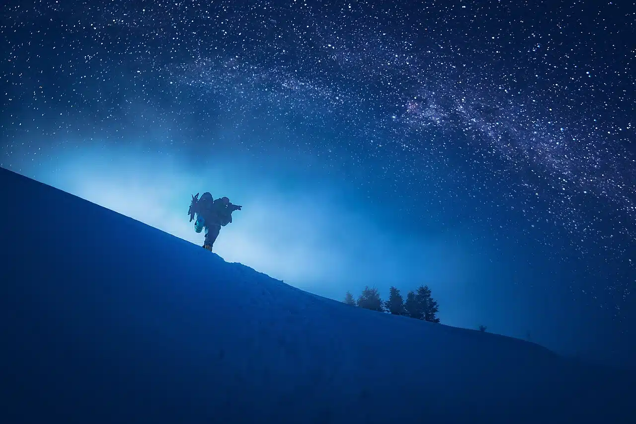 Silhouette d’un photographe sur une pente enneigée sous un ciel étoilé, voie lactée visible, nuit d’hiver.