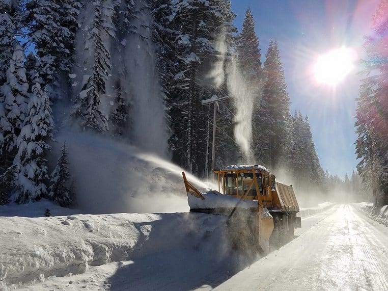 Camion chasse-neige en action sur une autoroute blanche, lame abaissée et neige projetée sur le bas-côté