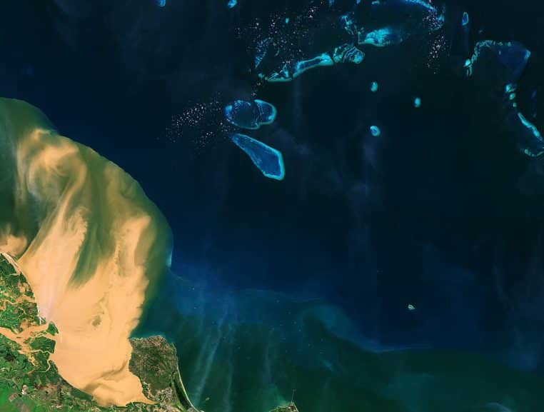 Image Sentinel-2 d’un panache de sédiments se déversant en mer près d’un récif, eau brunâtre et lagon bleu.