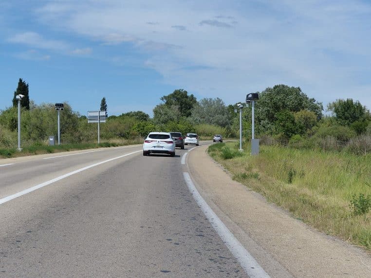 Route de campagne avec dispositifs de contrôle sur les bas-côtés, voitures en file et ciel dégagé