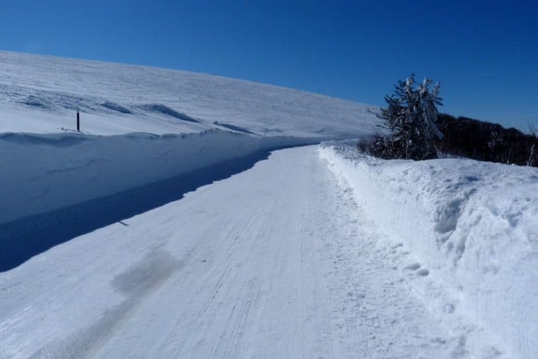 Chaussée de montagne recouverte de neige, bas-côtés blancs et route sinueuse, conditions hivernales marquées