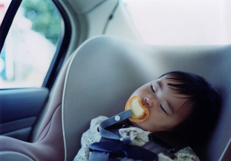 Enfant endormi dans un siège auto à l’arrière d’une voiture, photo en intérieur, cadrage horizontal.