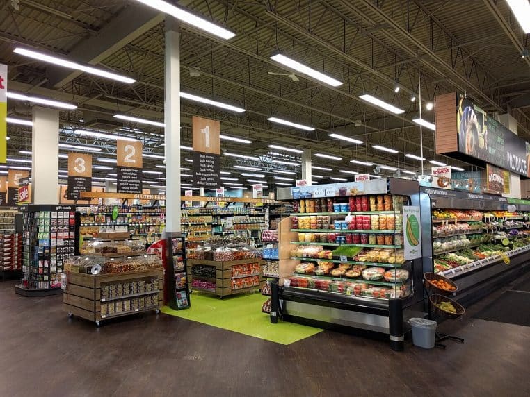 Rayons d’un grand supermarché avec étagères de produits emballés et éclairage industriel, vue large en intérieur.