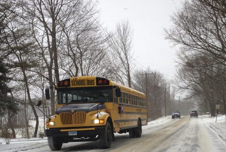 Bus scolaire roulant sur une route enneigée, circulation prudente au milieu des arbres d’hiver