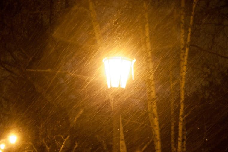 Neige poussée par le vent sous un lampadaire, scène nocturne dorée avec flocons visibles dans la lumière