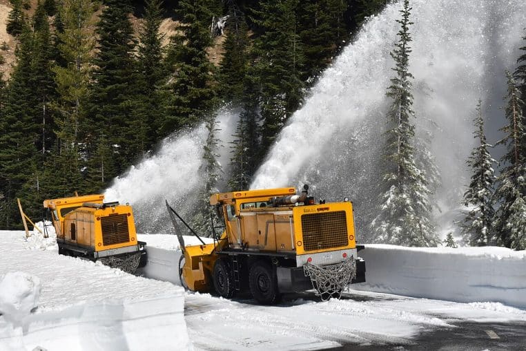 Engin de déneigement sur une route très enneigée, projection de neige et reliefs hivernaux en arrière-plan