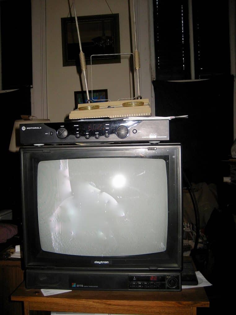 Téléviseur allumé dans un salon, canapé et meubles visibles, ambiance domestique, cadrage horizontal.