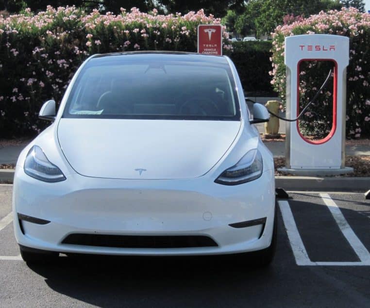 Tesla blanche en charge sur une borne rapide, câble branché, parking en arrière-plan