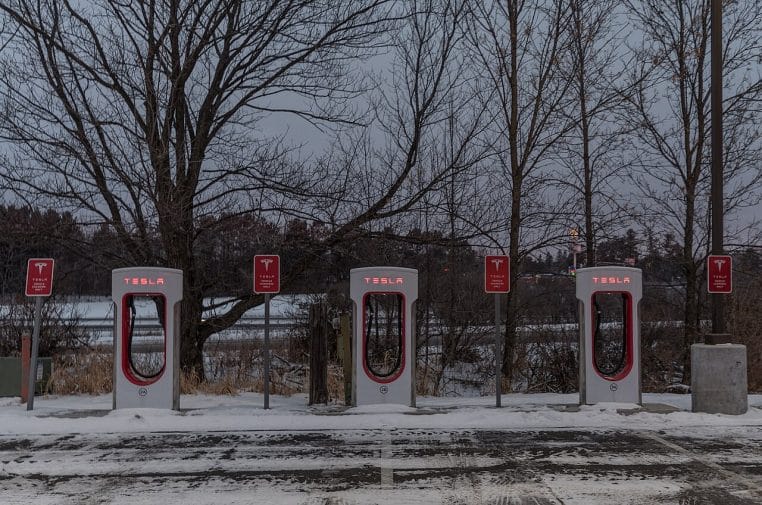 Station Tesla Supercharger alignée dans un paysage d’hiver, neige au sol et ciel froid, bornes visibles au premier plan.