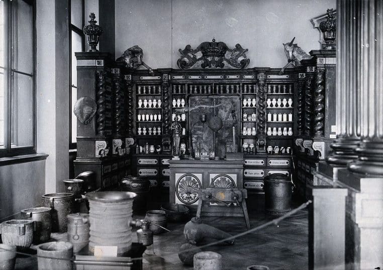 Intérieur d’une ancienne pharmacie avec étagères de flacons et comptoir, ambiance musée, vue d’ensemble.