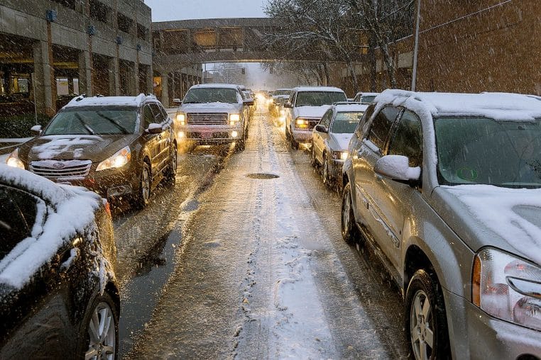 File de voitures immobilisées sur une autoroute enneigée, circulation à l’arrêt et flocons visibles