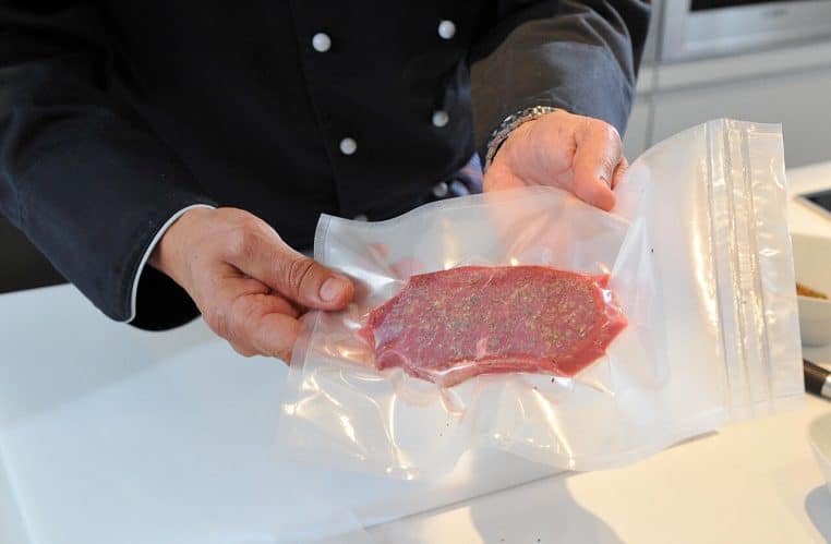 Mains tenant une pièce de viande dans un sachet transparent, prête à être emballée sous vide en cuisine.