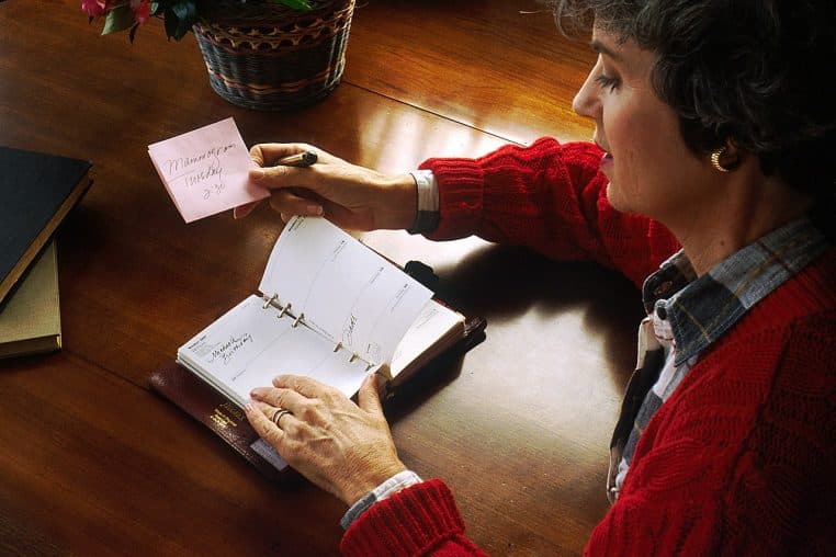 Femme assise à un bureau en train d’écrire un rendez-vous dans un carnet, stylo en main, scène de bureau