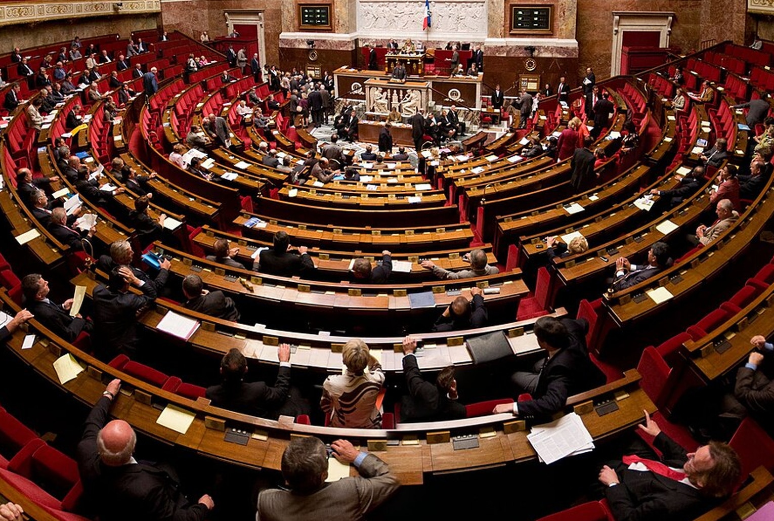 Vue panoramique de l’hémicycle de l’Assemblée nationale française, avec les bancs rouges et le perchoir au centre.