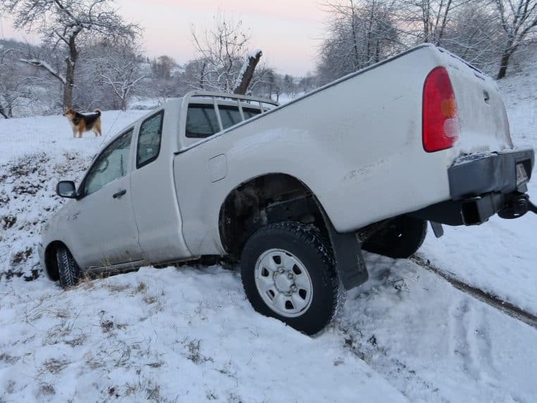 Pick-up blanc immobilisé dans un fossé enneigé, roues dans la neige et bas-côté glissant en hiver.