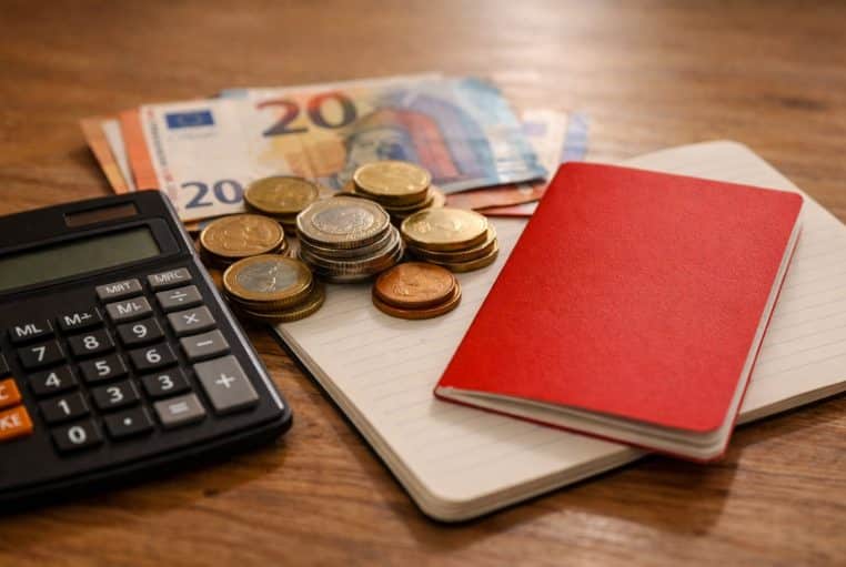 Calculatrice, pièces en euros et livret rouge sans inscription sur table, photo réaliste liée au Livret A.