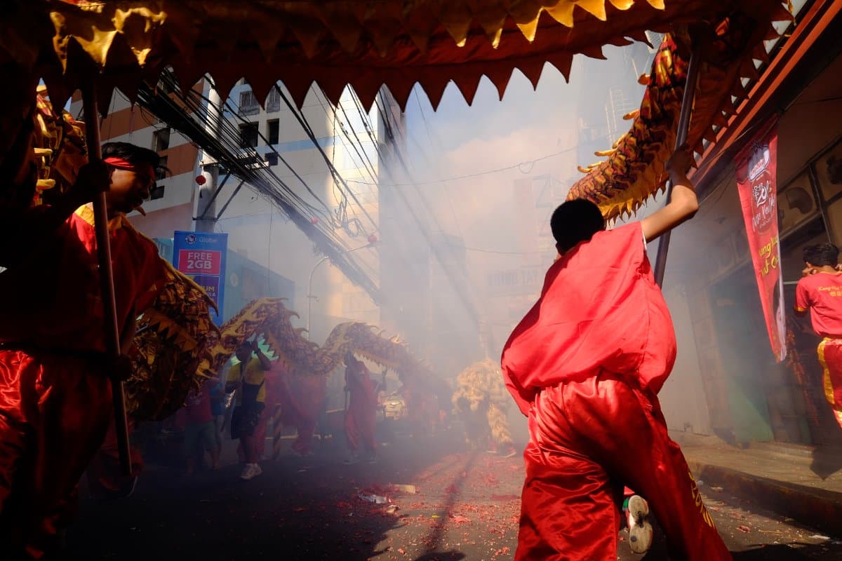 Danse du dragon dans une rue, avec fumée et participants en tenue rouge pendant une célébration du Nouvel An chinois.