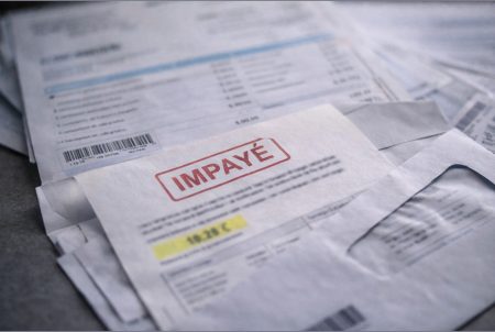 Factures et courriers empilés sur une table, avec une mention d’impayé, photo réaliste et neutre, sans marque.