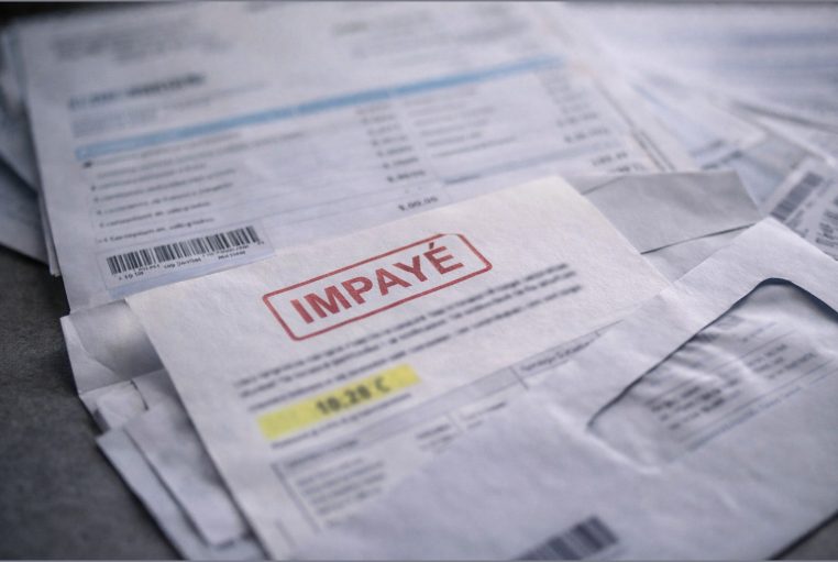 Factures et courriers empilés sur une table, avec une mention d’impayé, photo réaliste et neutre, sans marque.