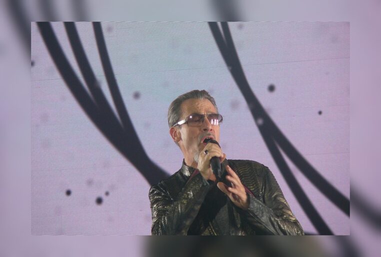 Florent Pagny en concert, gros plan au micro, lunettes, veste brillante