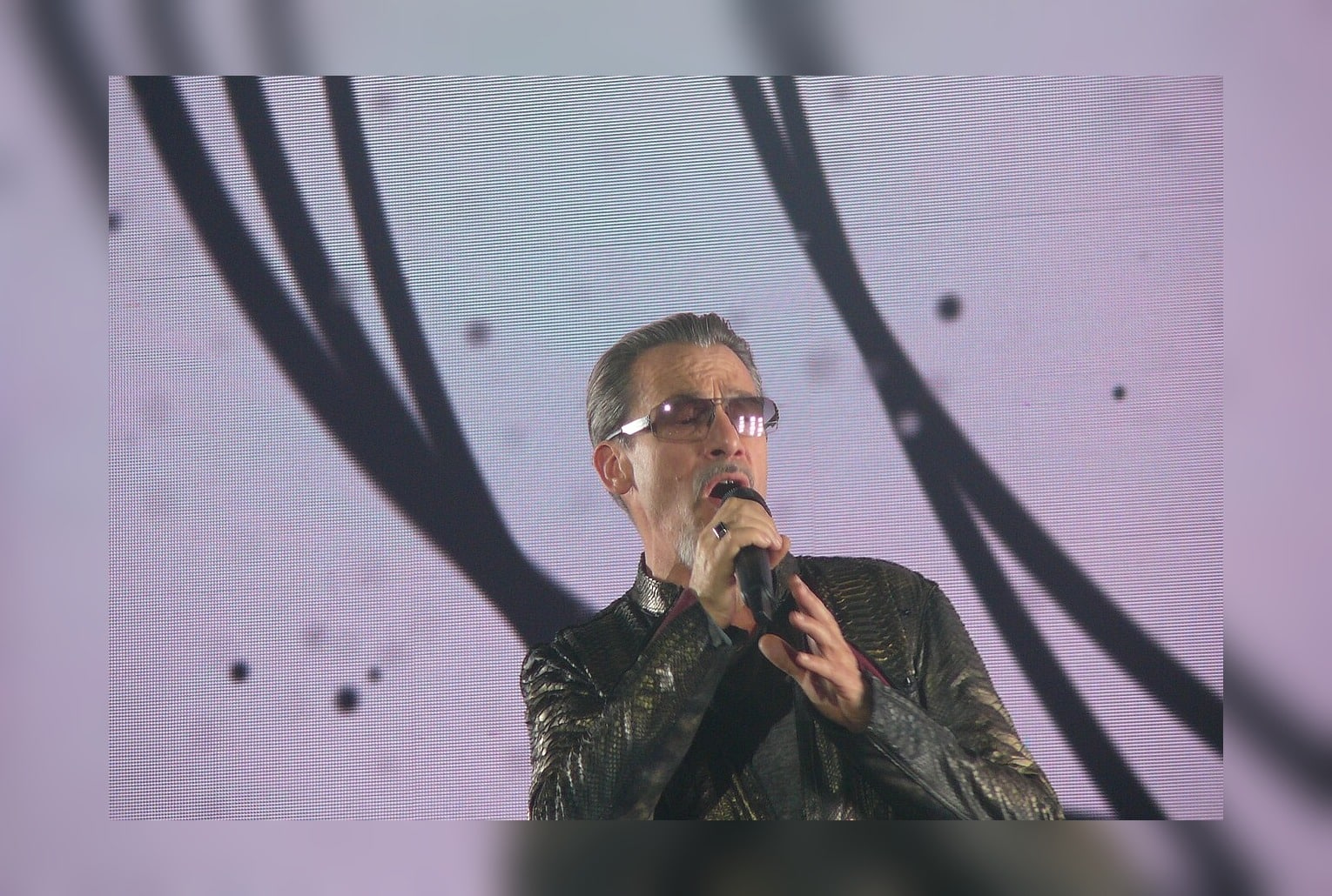 Florent Pagny en concert, gros plan au micro, lunettes, veste brillante