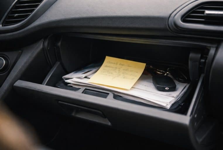 Boîte à gants ouverte d’une Ford avec un post-it manuscrit posé sur des papiers et un jeu de clés.