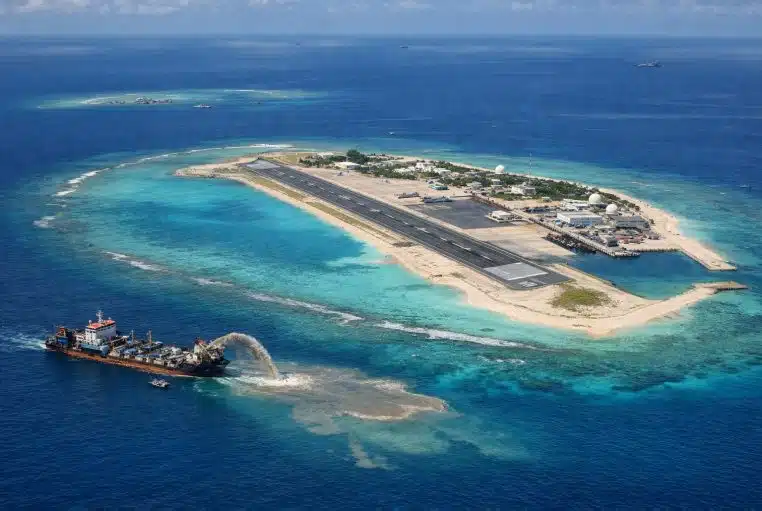 Vue aérienne d’une île artificielle avec piste et port, entourée d’un lagon turquoise en mer de Chine.