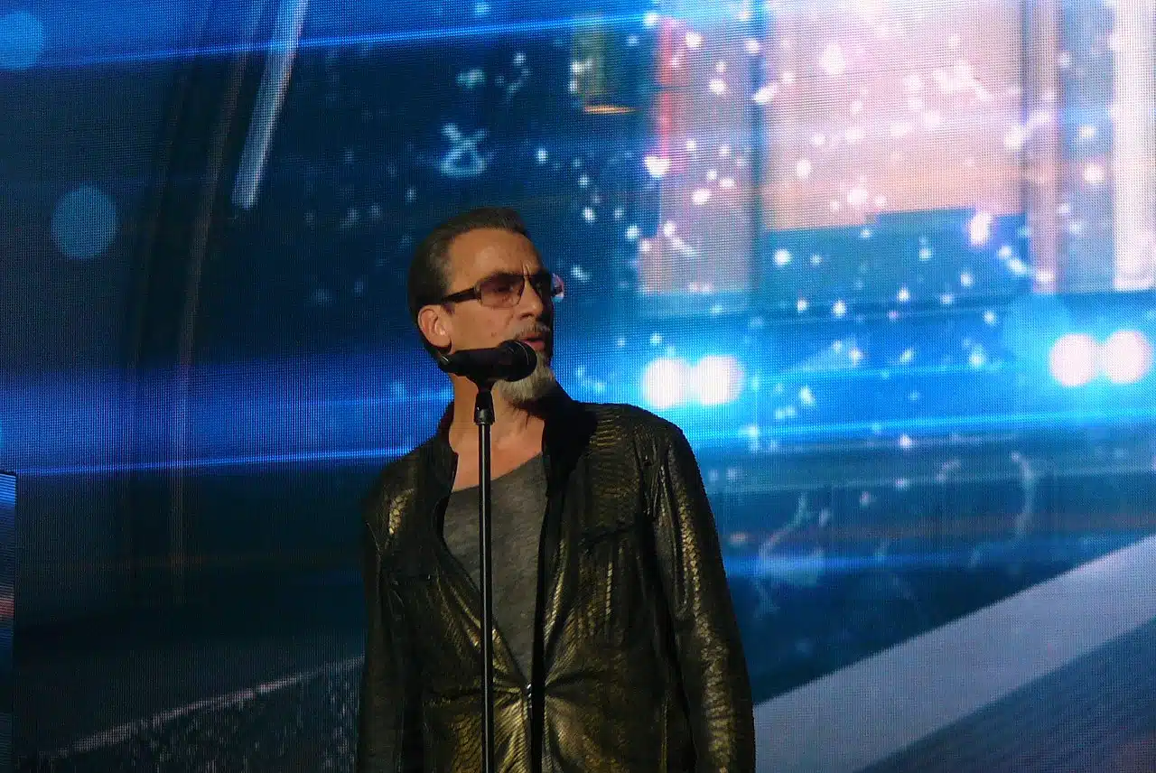 Florent Pagny en concert, gros plan au micro, lunettes, veste brillante