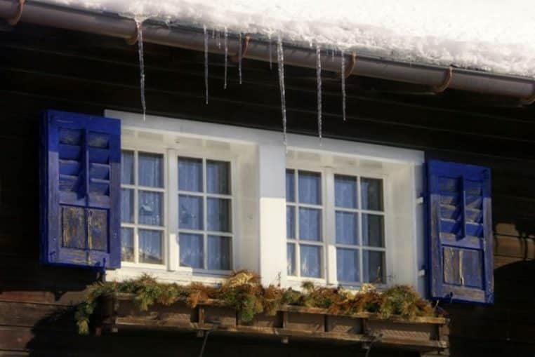 Fenêtre avec volets bleus, neige et stalactites en hiver.