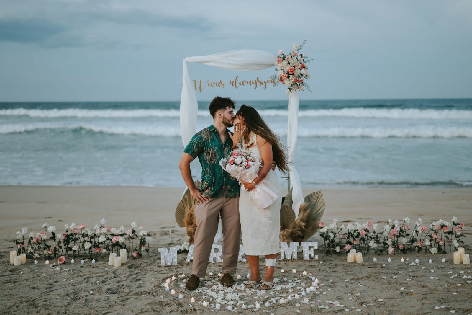 Couple posing on a beach during a proposal setup.