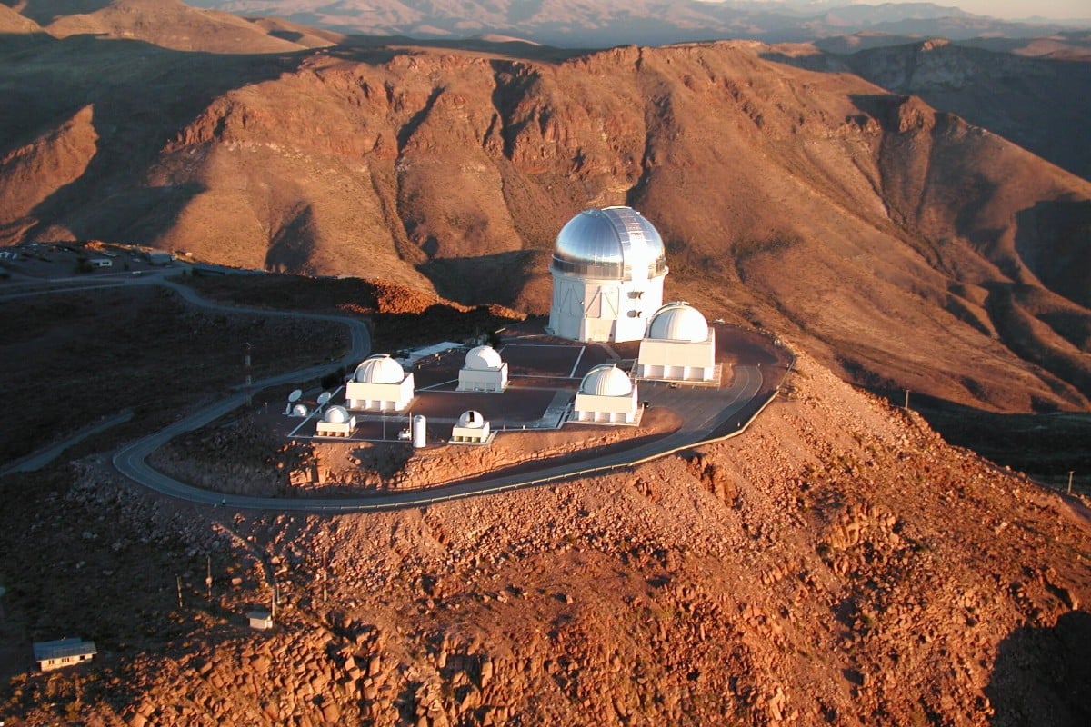 Vue aérienne panoramique de l'observatoire de Cerro Tololo (Chili), avec plusieurs dômes de télescopes sur une crête aride.