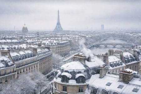 Vue panoramique de Paris sous la neige, avec la tour Eiffel au centre et des toits haussmanniens blanchis au premier plan.