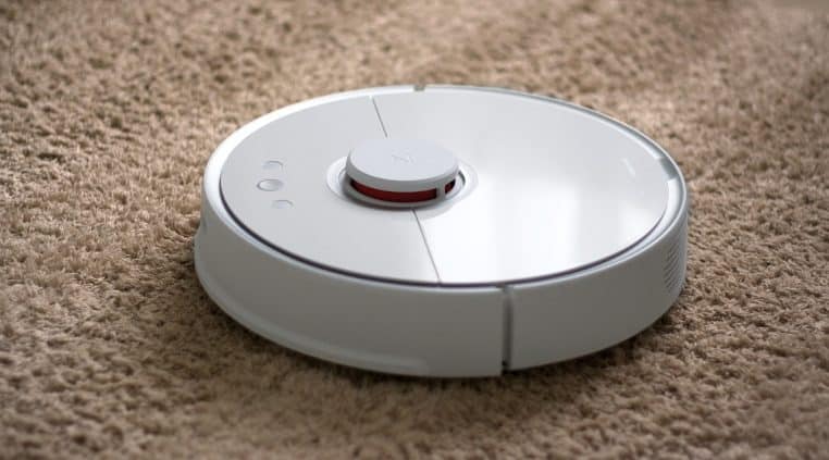 Robot aspirateur circulaire avançant sur un tapis, photo horizontale illustrant le nettoyage automatique au quotidien.