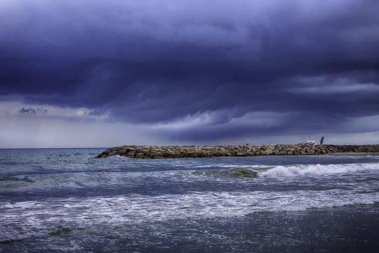 Ciel d’orage très sombre au-dessus d’une digue, mer formée et vagues sur une plage exposée au vent