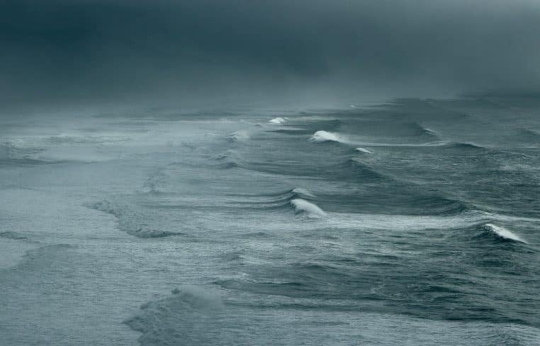 Large houle et embruns sur l’océan sous un ciel gris, conditions typiques de tempête et rafales de vent