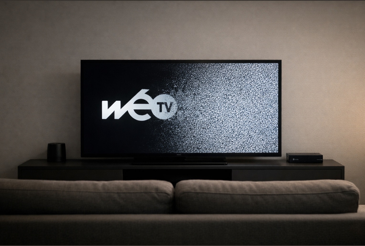 Salon sobre avec une télévision où le logo Wéo TV s’efface, remplacé par du bruit blanc.
