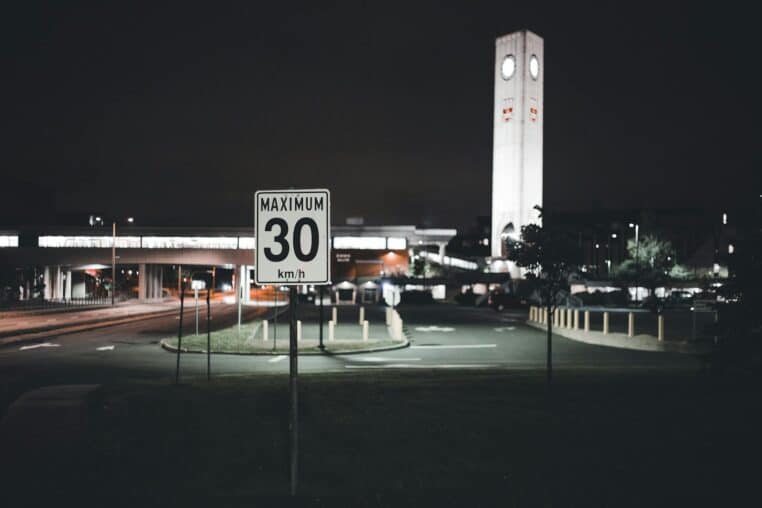 A city street at night featuring a speed limit sign and an illuminated clock tower, creating an urban atmosphere.