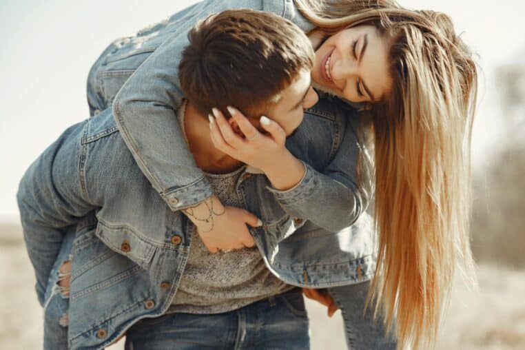 A joyful young couple in denim sharing a playful piggyback ride in a sunny meadow.