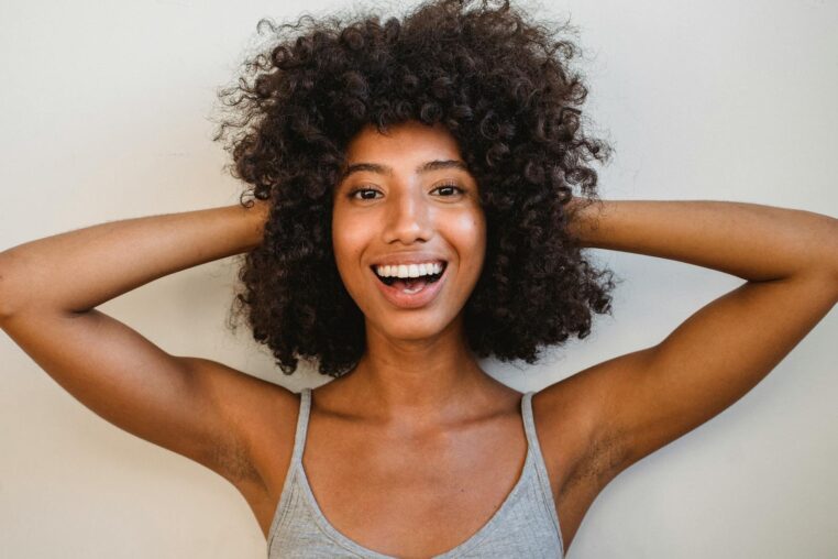 A cheerful African American woman with curly hair smiling confidently at the camera.