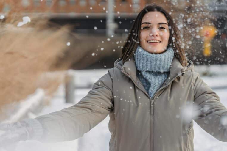 A cheerful young woman in a winter coat, enjoying a snowy day outdoors.