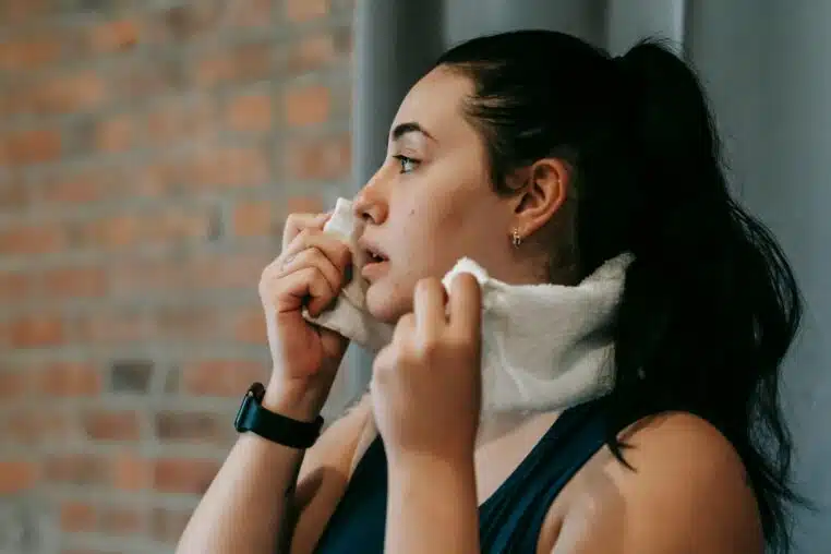 Side view of a woman wiping sweat with a towel after exercising indoors.