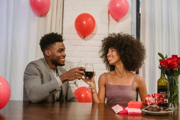A joyful couple celebrating Valentine's Day with wine and decorations in a cozy setting.