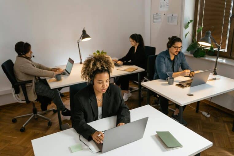 Diverse team of call center agents working at computers in an office setting, focused on tasks.